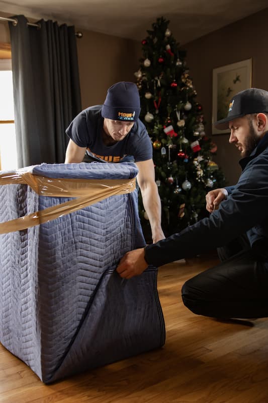 Two Move and Care movers wrapping a dresser in a moving blanket