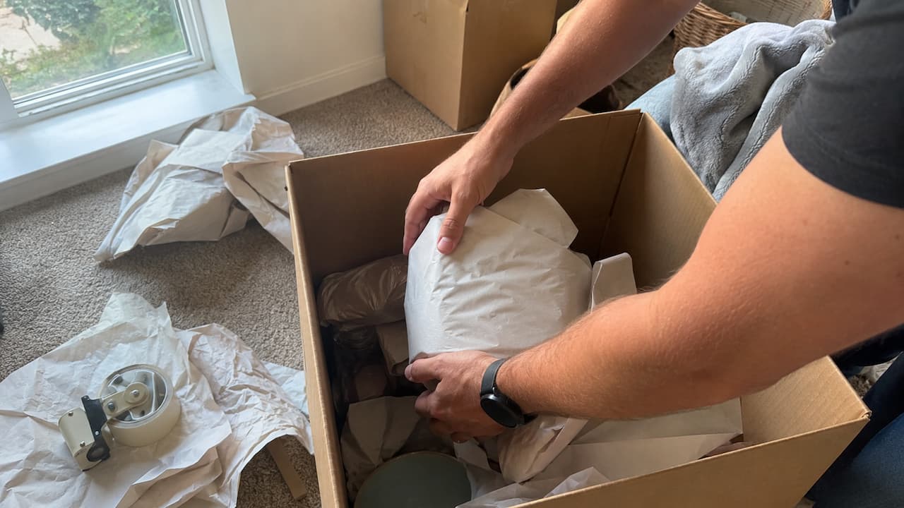 Person packing wrapped household items into a cardboard box for interstate shipping