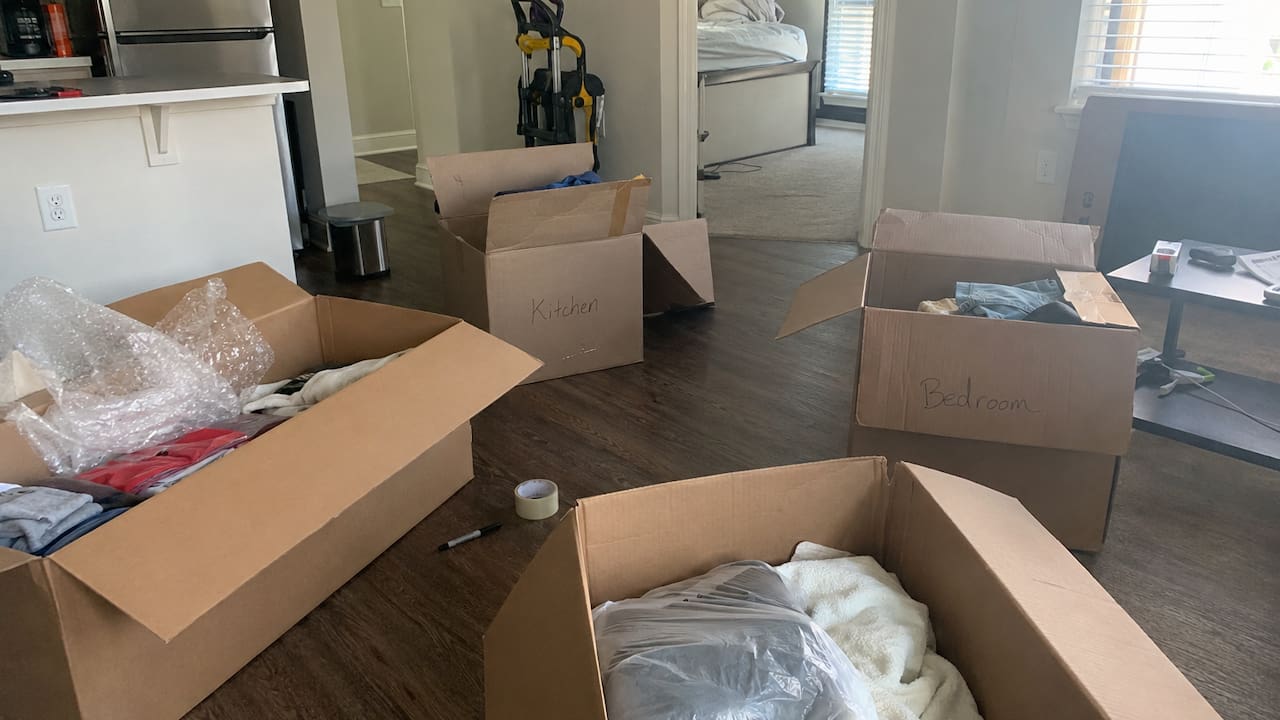 Labeled moving boxes, packing tape, clothes, and household items prepared for a move